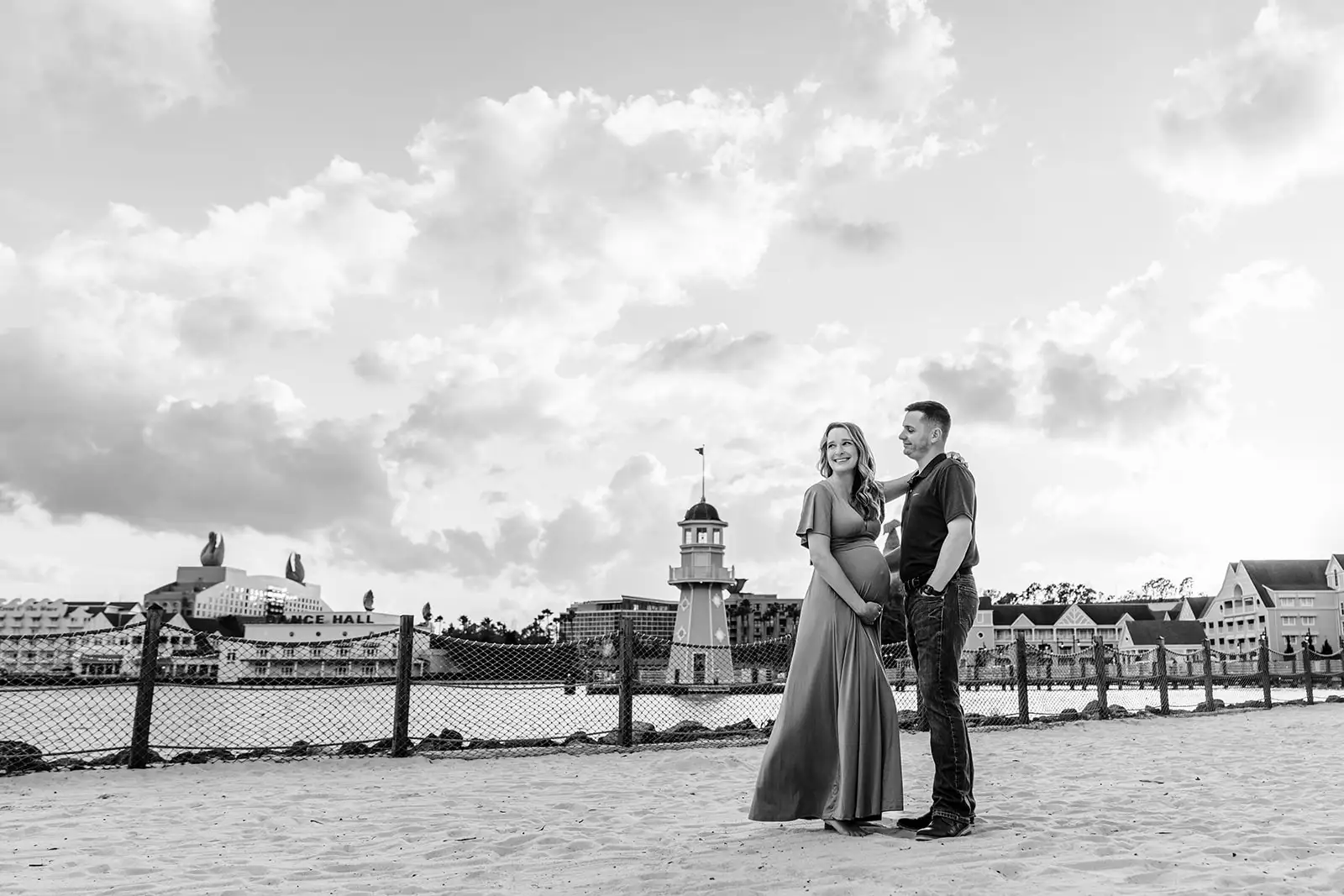 Man and woman in maternity photo at Disney Boardwalk with lighthouse in background