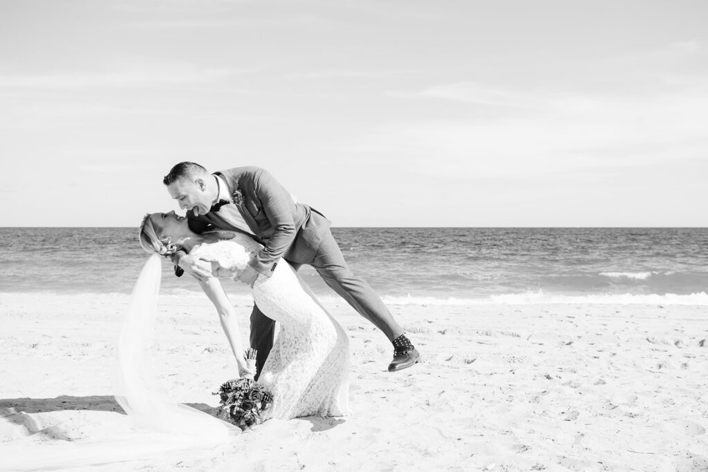 black and white photo of groom dipping bride on beach