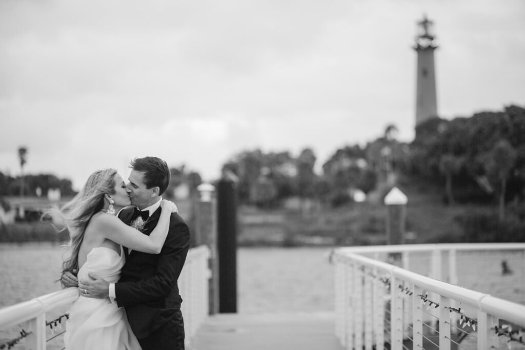 black and white photo of bride and groom kissing by lighthouse