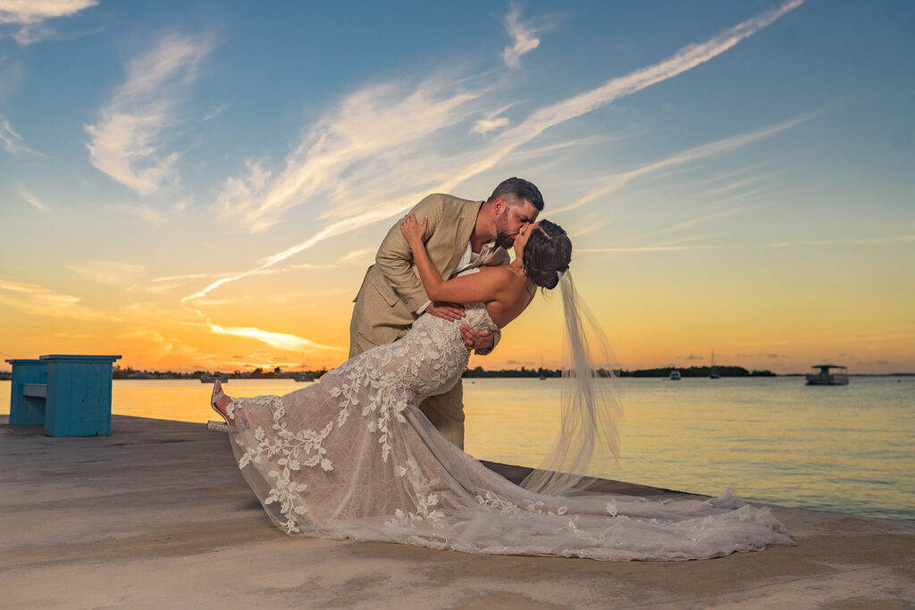 groom dips bride at sunset by ocean