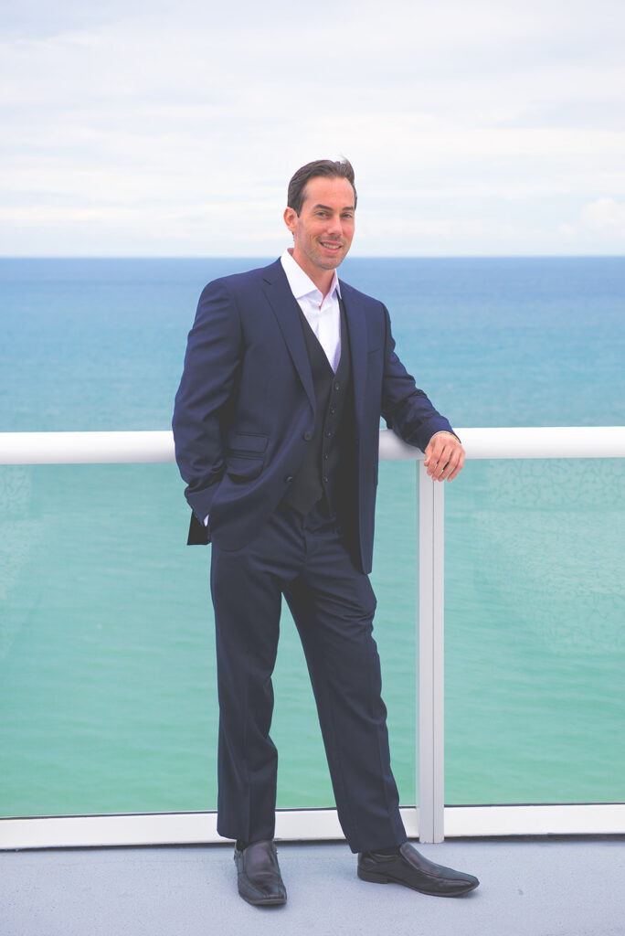 groom leans on rail by the ocean