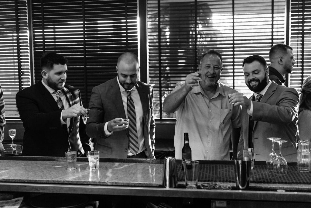 black and white photo of men at wedding having shots at bar