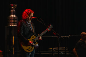 man playing guitar, standing in a dark room with red lighting