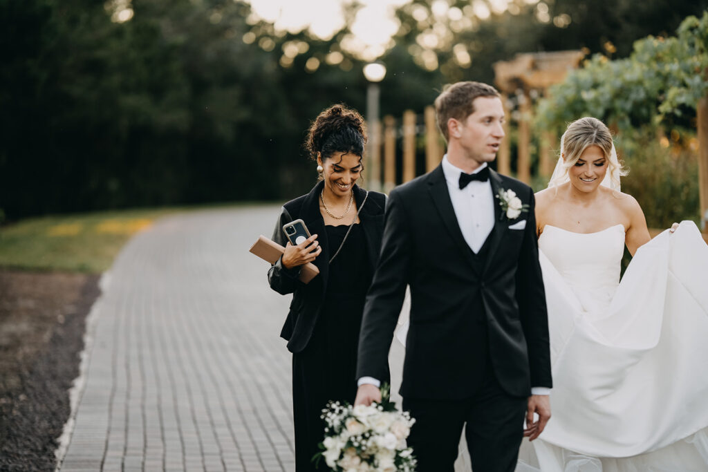 Wedding planner walking behind bride and groom on brick paver path