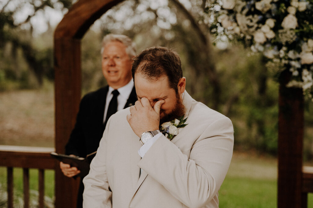 Groom crying when he sees his bride walking down the aisle at an outdoor wedding