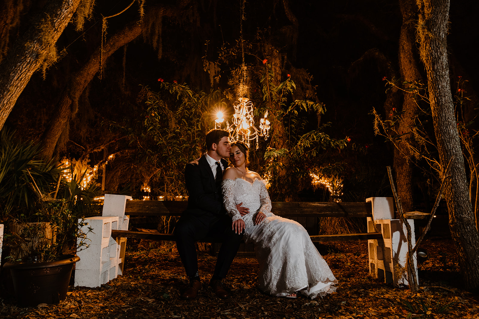 Bride and groom sitting under a tree under a chandelier