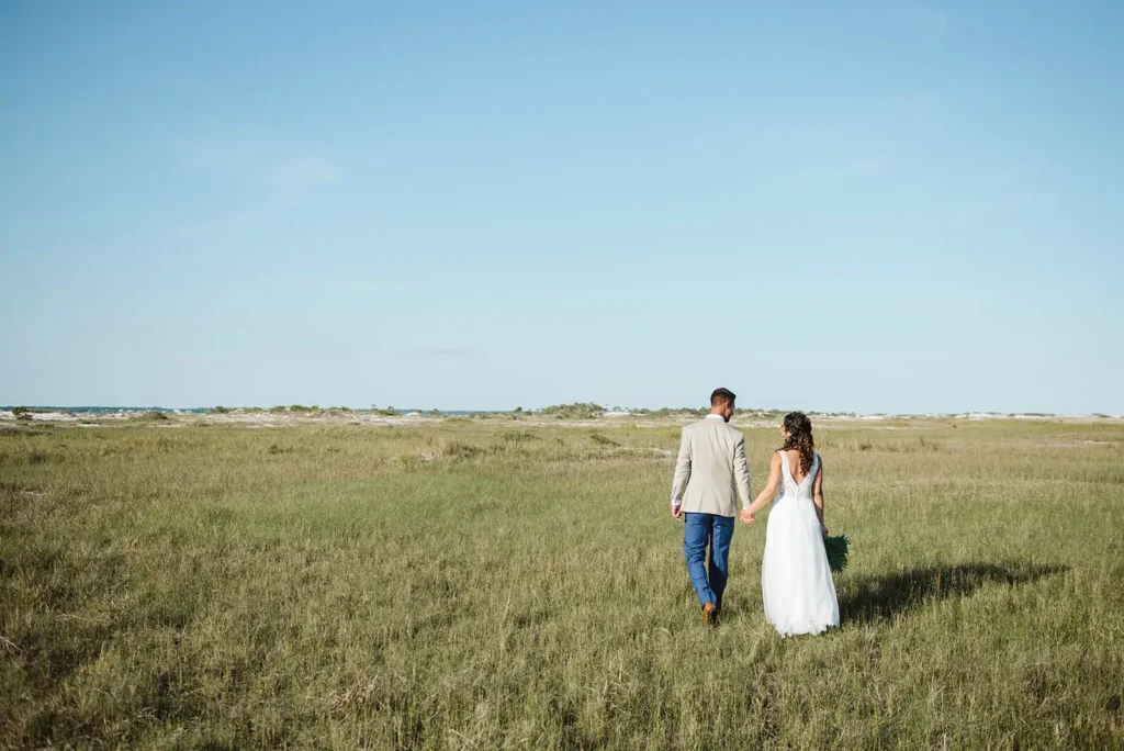 Bride and groom walking in large green space by beach in Pensacola, FL