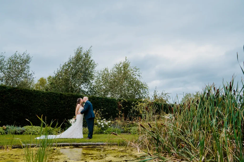 Bride and groom in lush garden by water at UK destination wedding venue