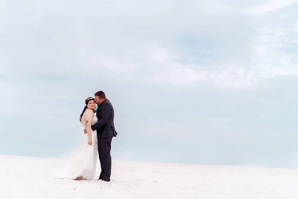 Groom kisses bride white sand beach