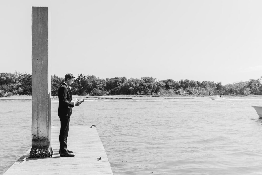 black and white groom by water reading letter from bride