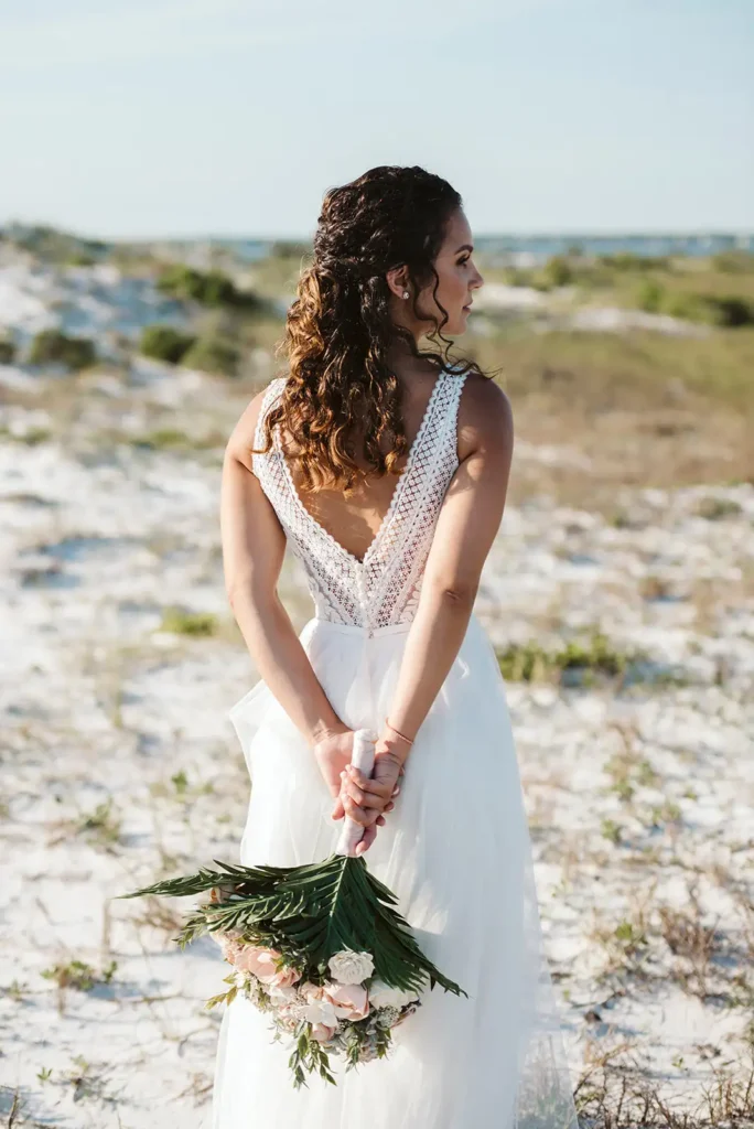 bride holding bouquet behind back on beach