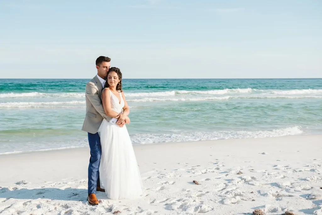 Bride and groom hug on beach near ocean