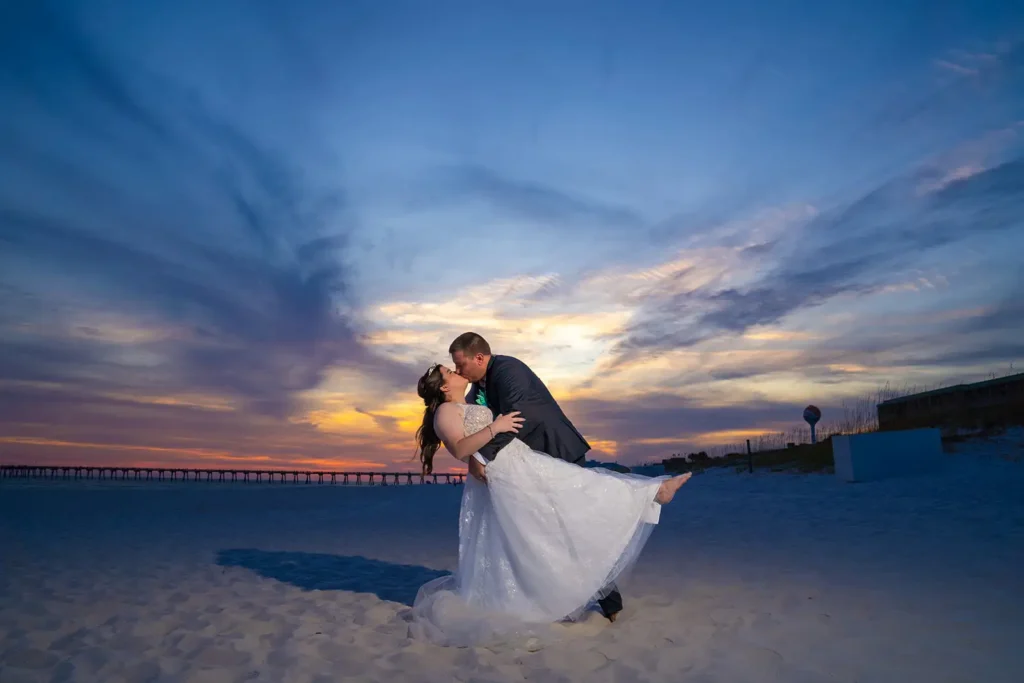 Groom dips bride on beach at sunset
