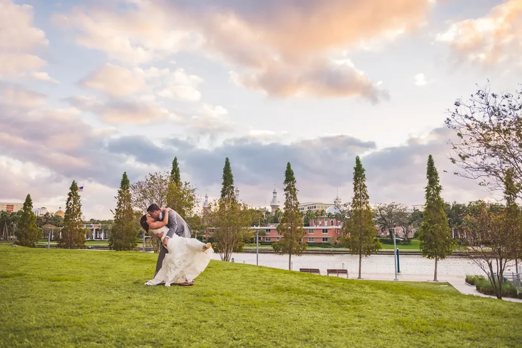 Groom dips bride in a park by the water
