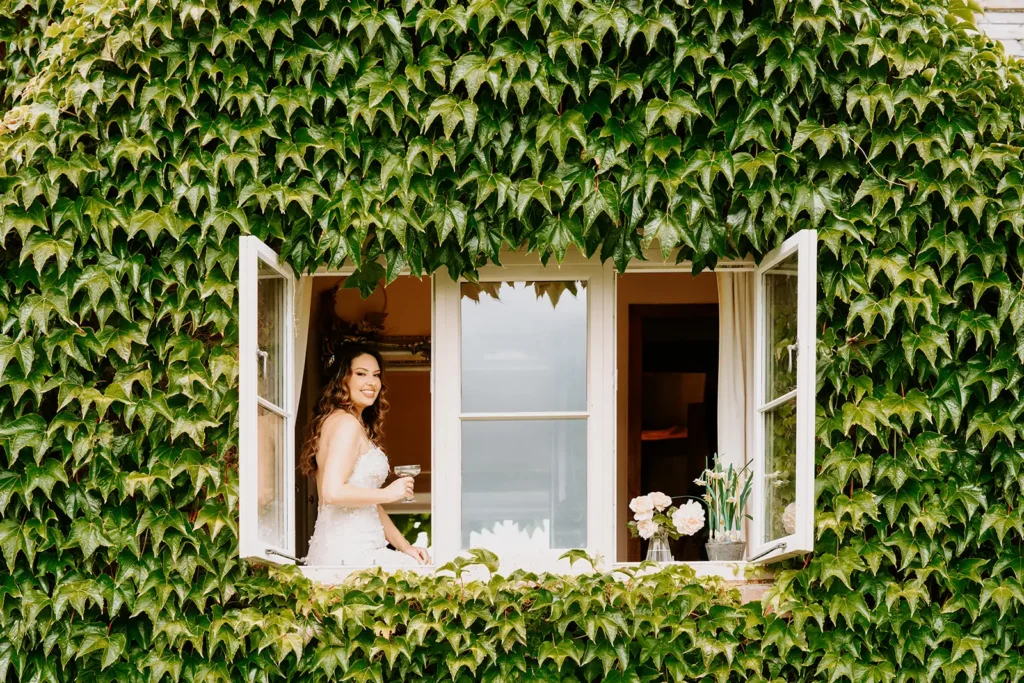 Bride sitting in open window in wall covered with large green vine
