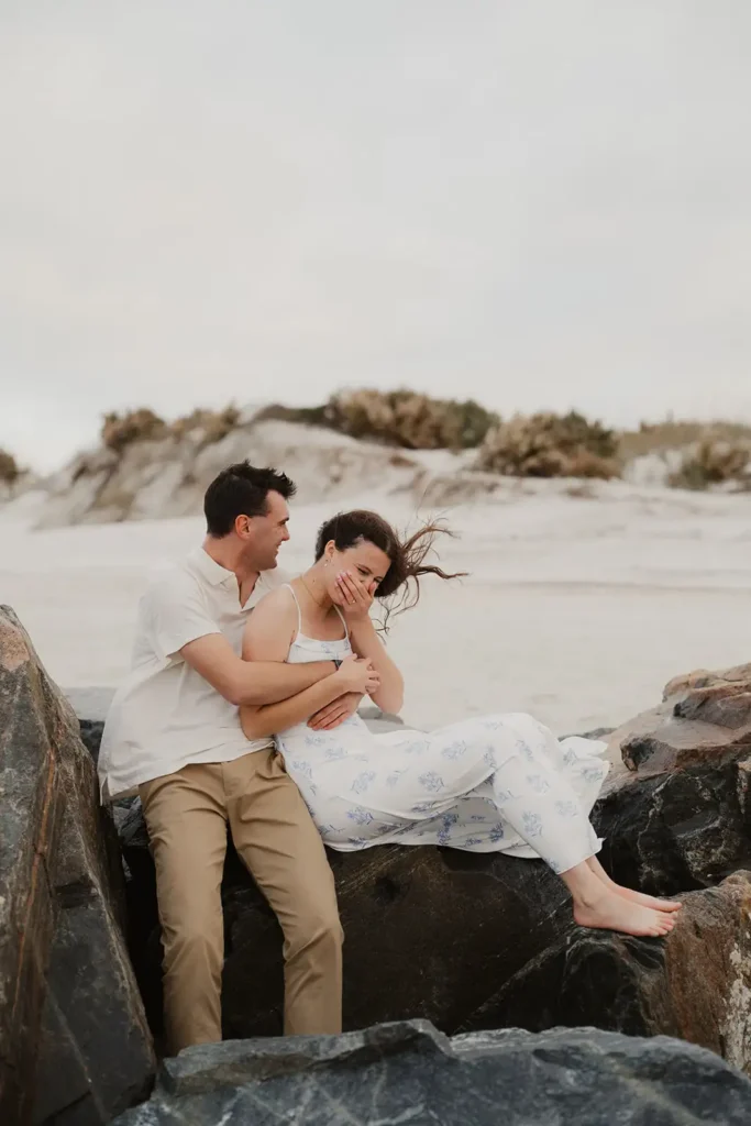 couple laughing sitting on rocks on beach