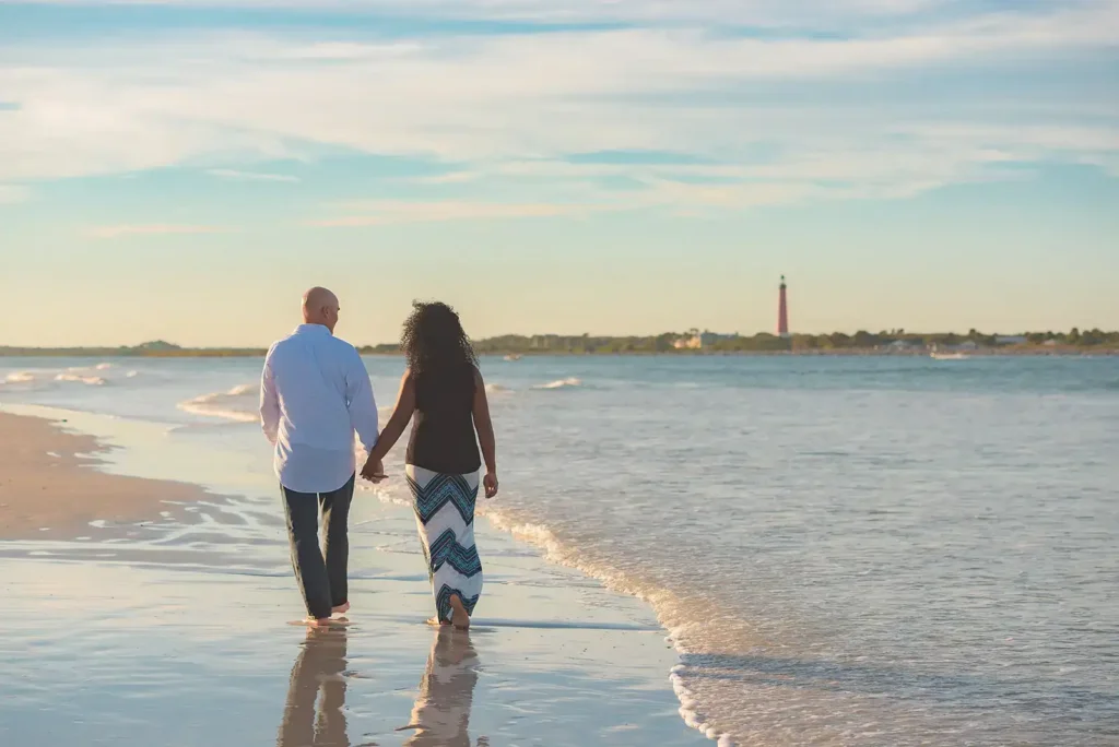 Man and woman walking in surf with lighthouse in background