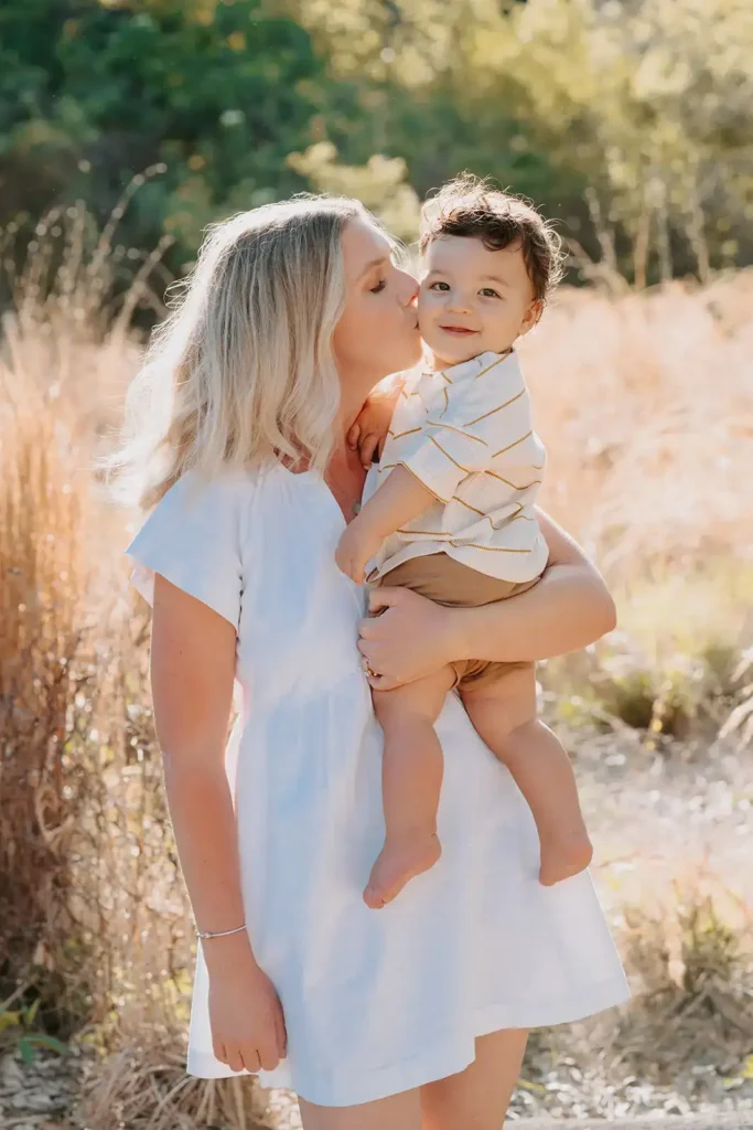 Mom kisses young son outside in a field