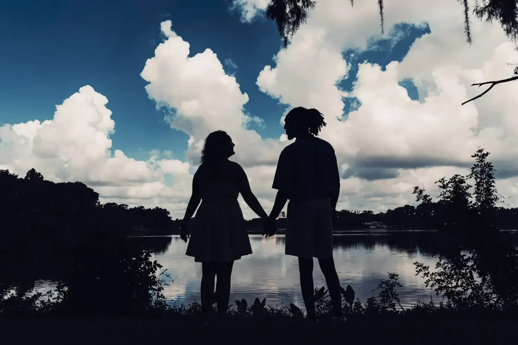 couple at waters edge silhouetted by blue sky and clouds