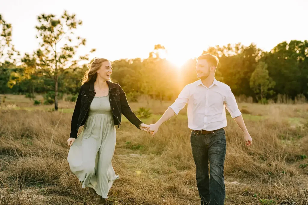 couple hodling hands with sun setting behind trees