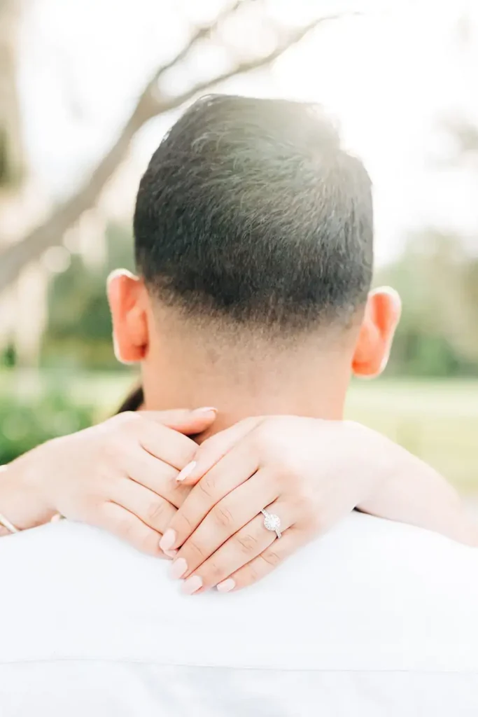 Back of man's head with woman's hands around neck showing engagememnt ring