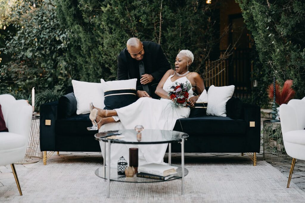 Groom sitting on black couch with groom leaning over back