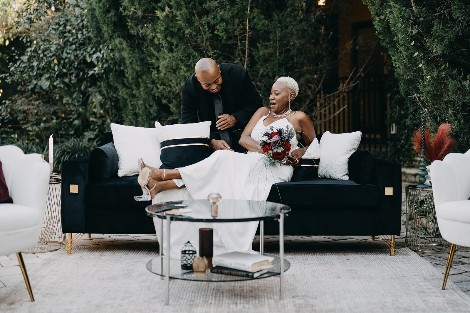 Groom sitting on black couch with groom leaning over back
