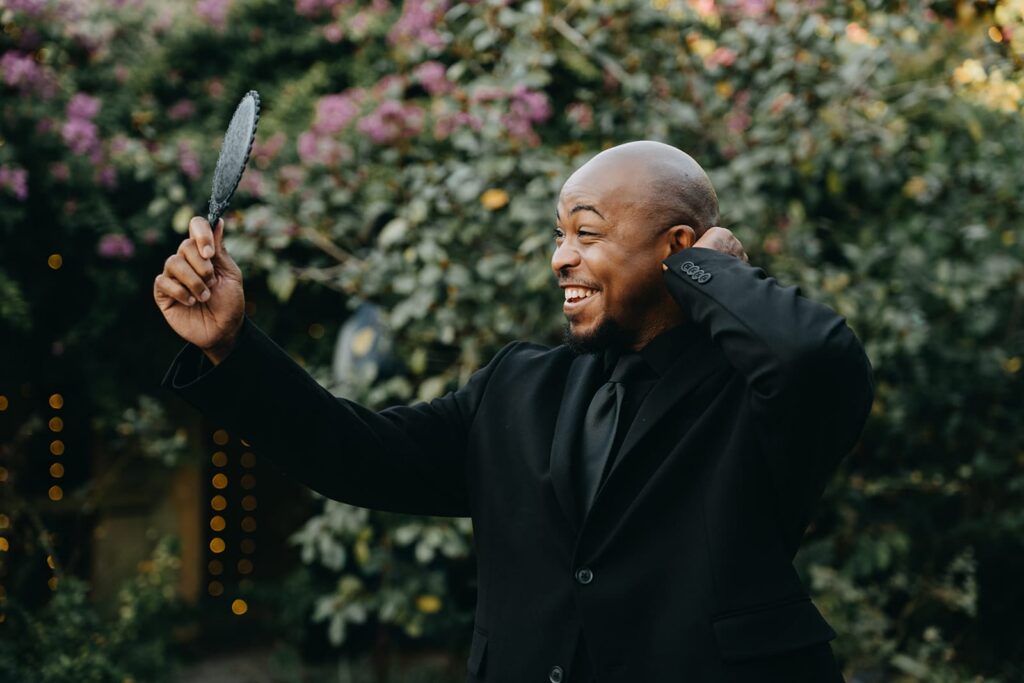 Groom smiling at himself in a handheld mirror