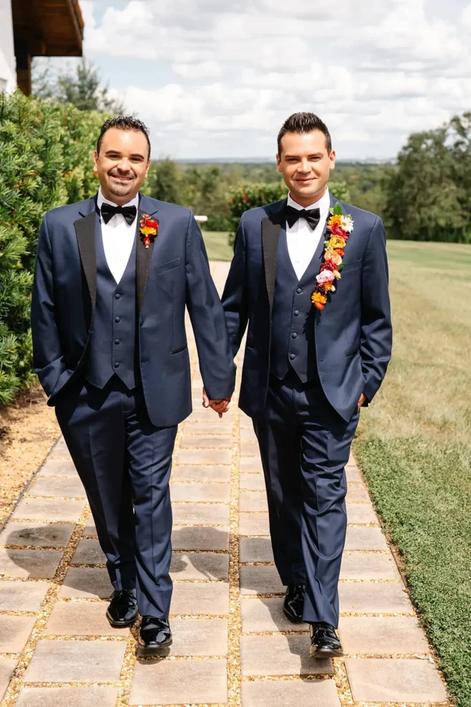 2 grooms with floral accessories walk hand in hand